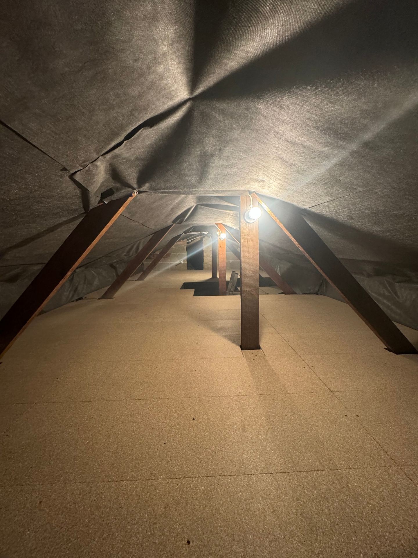 Dimly lit attic space with wooden beams and exposed insulation.