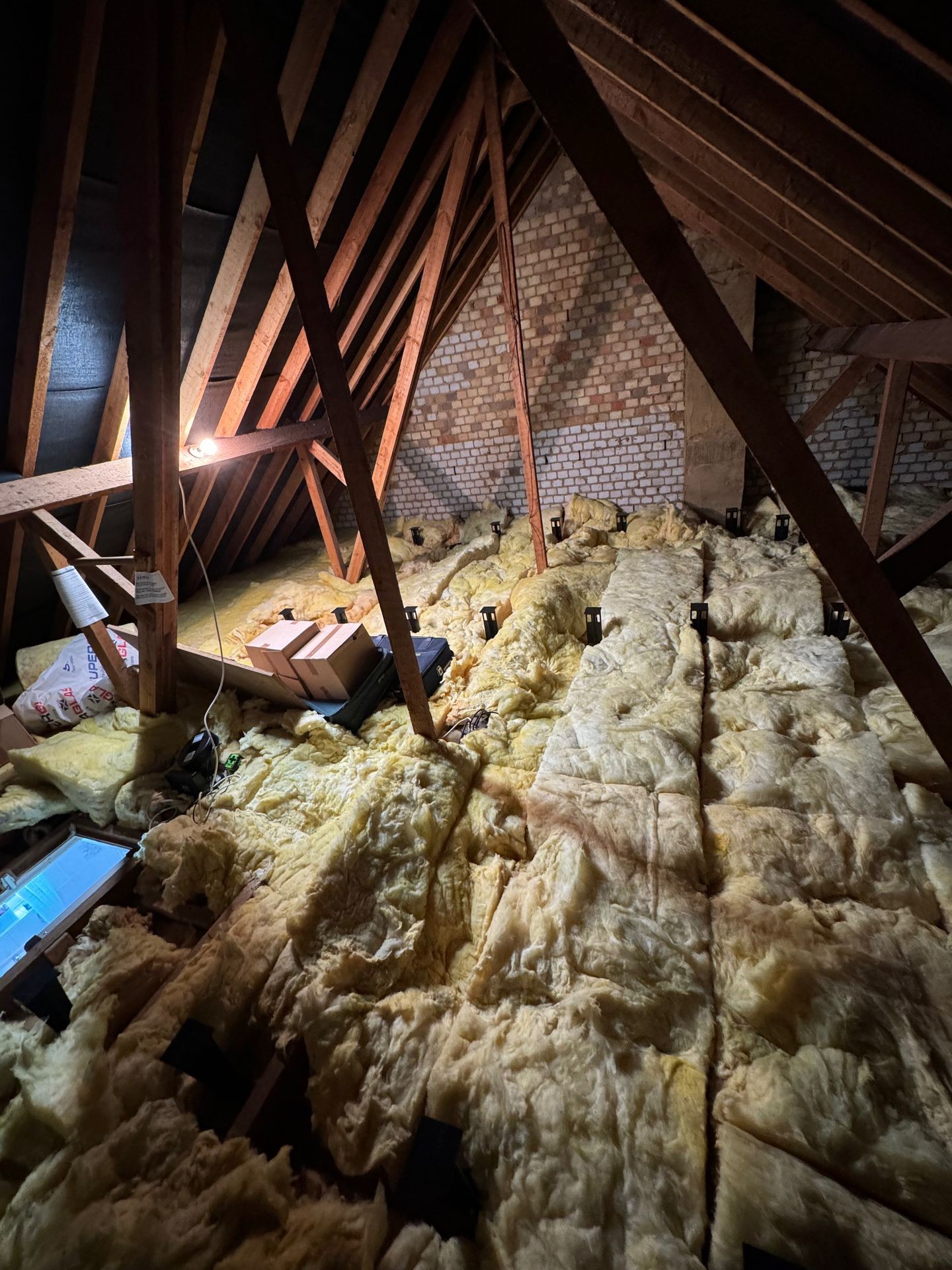 Attic space with exposed beams and yellow insulation covering the floor, dimly lit.