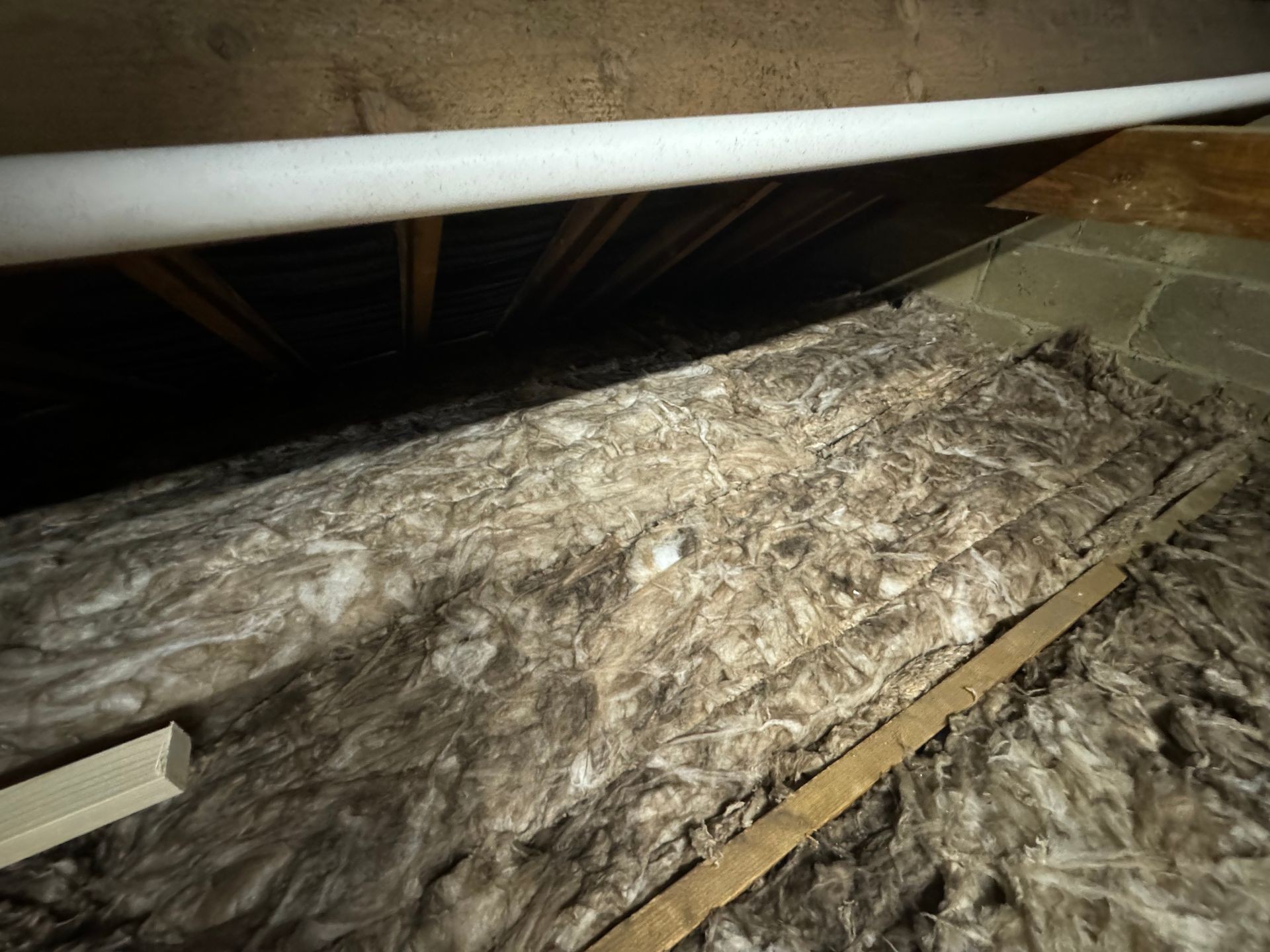 Attic with exposed insulation material and supporting wooden beams.