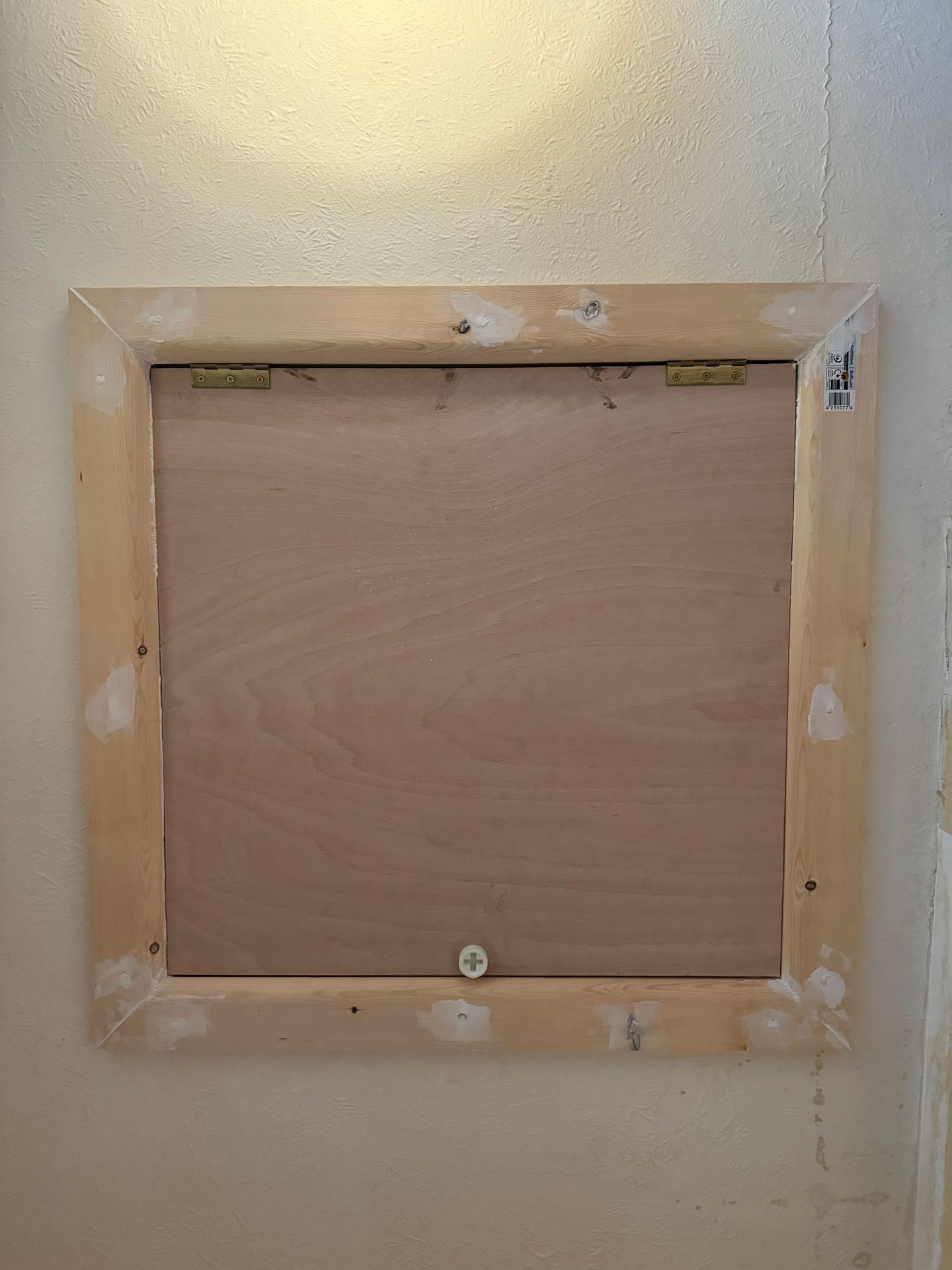 Wooden framed panel with hinges mounted on a textured wall, concealing an access point.