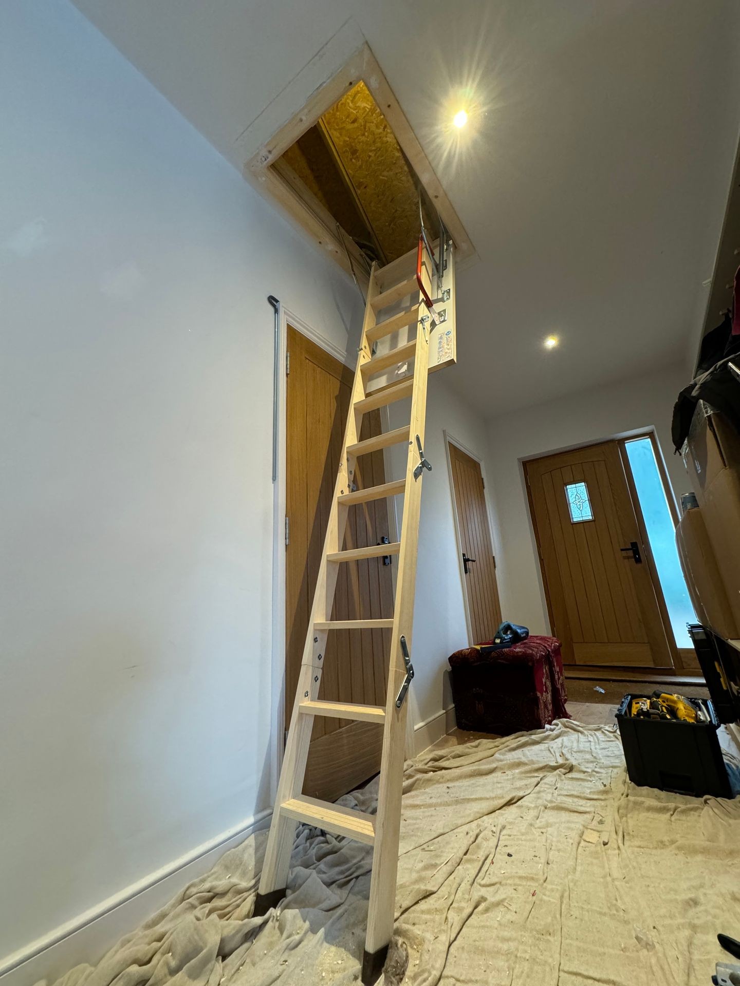 Wooden ladder extending to attic in a hallway with wooden doors and a toolbox on the floor.